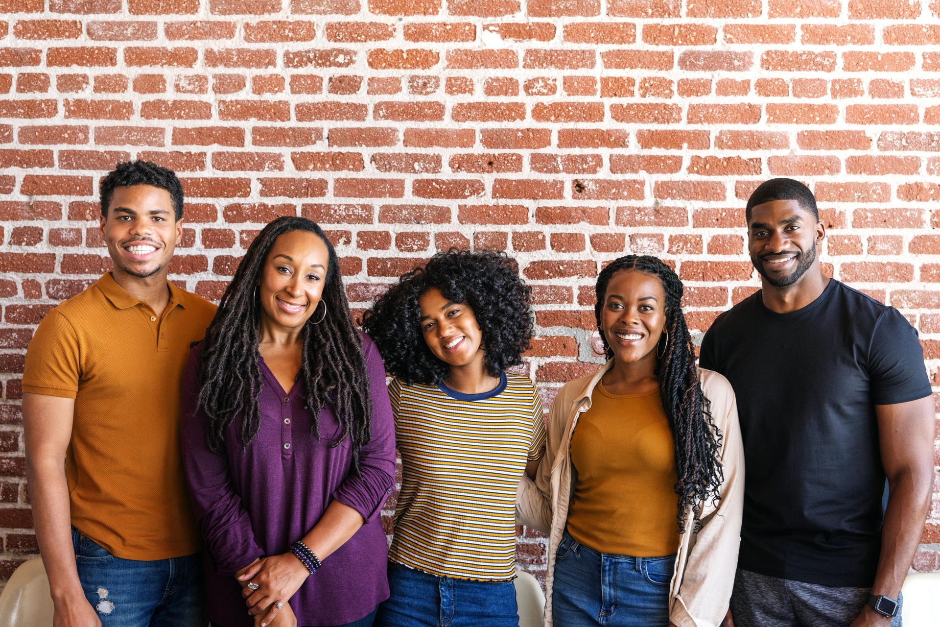 Group of five people smiling in front of a brick wall.
